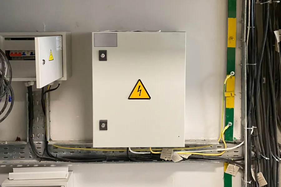 Electrical panel with cables and hazard sign.